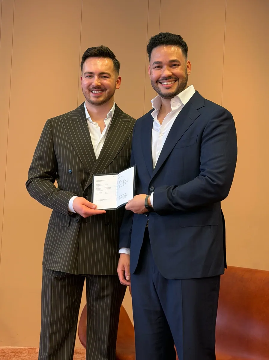 Klaudio and Derick dressed in suits, holding their official document together